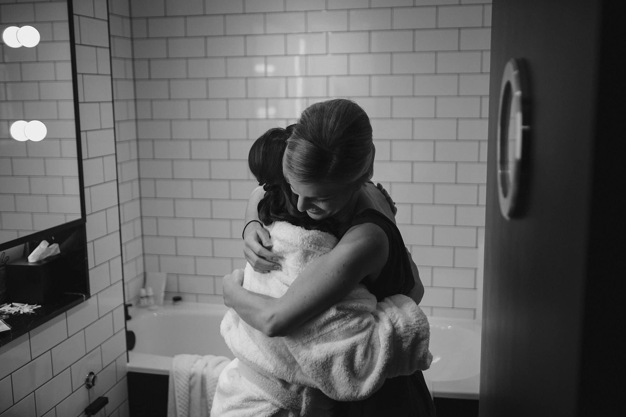 bride and bridesmaid hugging in bathroom