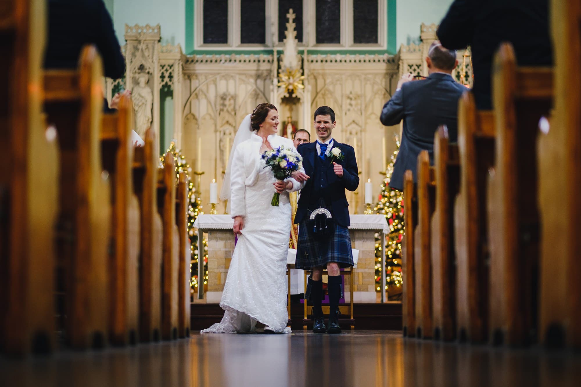 a low-angle wedding photograph showing a grinning bride and groom walking down the aisle after getting married