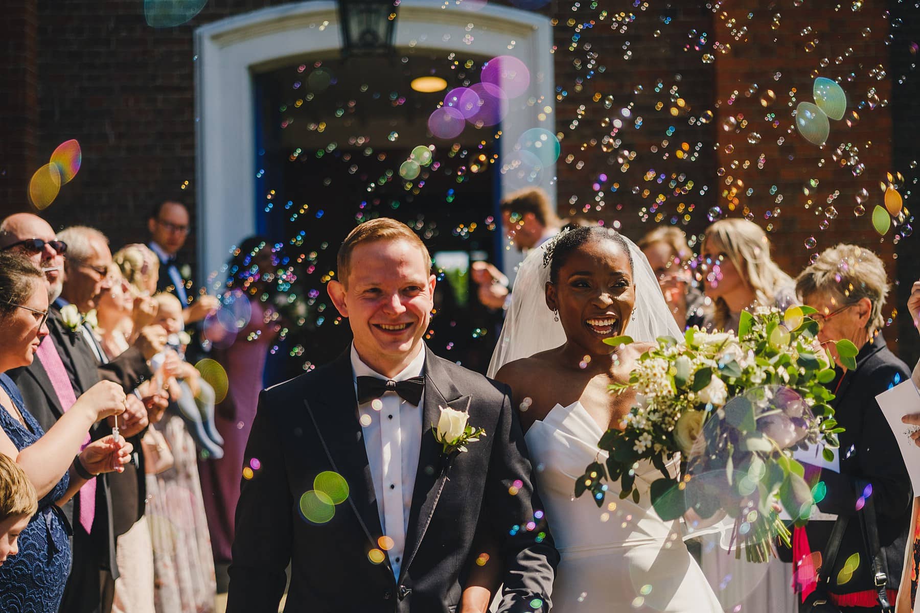 bride and groom grinning as guests blow bubbles as they leave the church during a london wedding